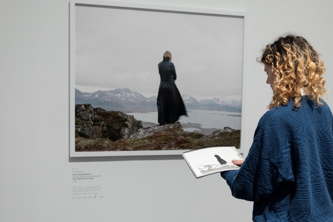 Eine Frau steht vor der Fotografie Der Wanderer II aus der Serie the New Painting, 2004 von Elena Brotherus. In ihren Händen hält sie eine Tastkopie zur Fotografie, die sie mit einer Hand ertastet. Hamburger Kunsthalle,Foto: Fred Dott