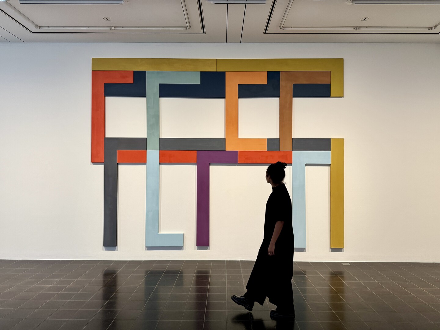Person geht in einer Galerie vor großem bunten geometrischem Gemälde vorbei