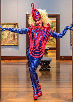 Farbenfroh gkleidete Drag Queen in Tanzpose in einer Kunstgalerie