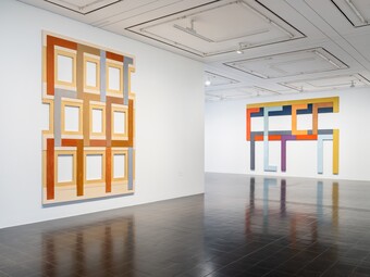 Gallery with illuminated wall objects in orange frames and a dark floor
