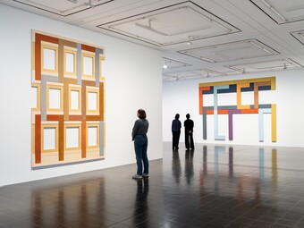 Three people are looking at works of art in a gallery