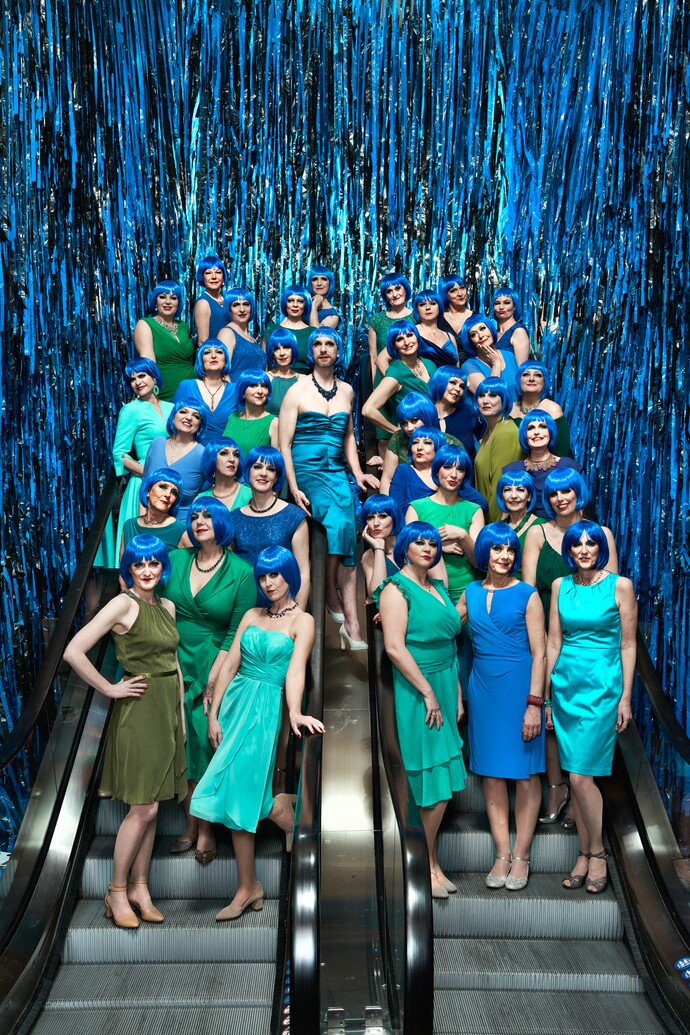 Gruppe von Frauen in blauen Kostümen und Perücken posiert vor glänzendem blauen Vorhang