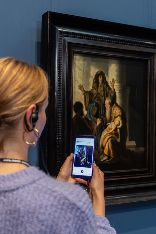 Eine Frau mit Handy und Kopfhörern vor dem Gemälde von Rembrandt Harmensz. van Rijn (1606–1669)