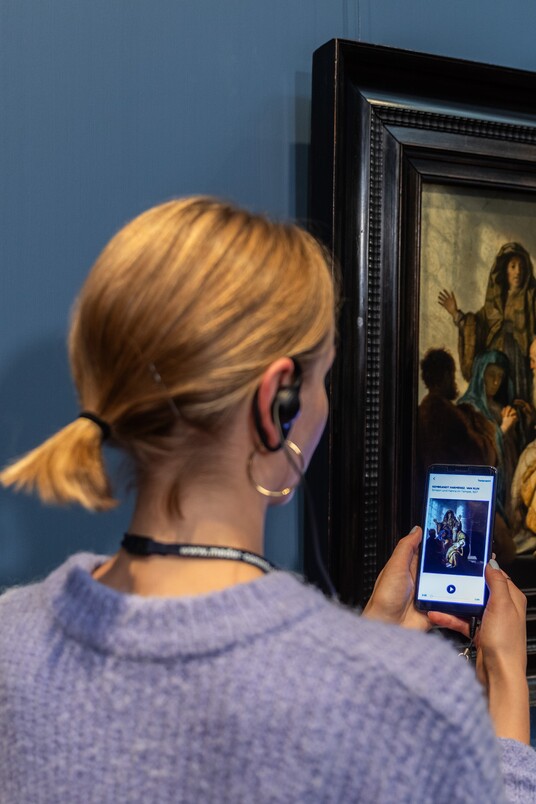 Eine Frau mit Handy und Kopfhörern vor dem Gemälde von Rembrandt Harmensz. van Rijn (1606–1669)
