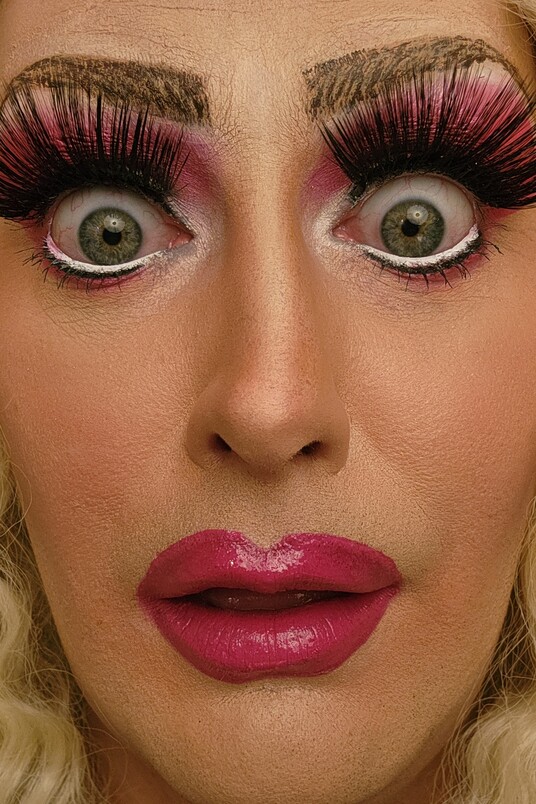 Drag mit dramatischem Make-up, langen künstlichen Wimpern und pinkem Lippenstift