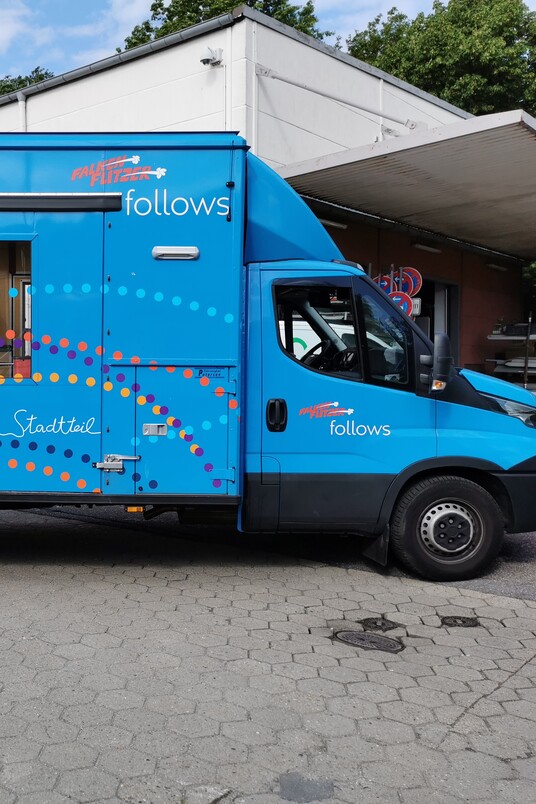 Blauer Truck mit Bedienungsfenstern auf der Seite, geparkt auf einem Platz