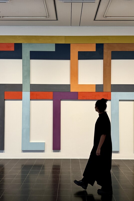 Person geht in einer Galerie vor großem bunten geometrischem Gemälde vorbei