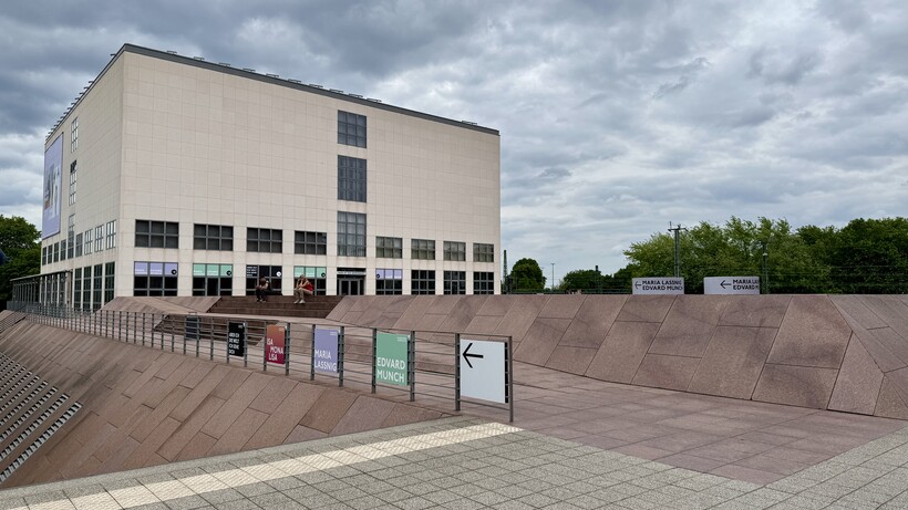 Modernes weißes Gebäude mit gepflastertem Vorplatz unter bewölktem Himmel