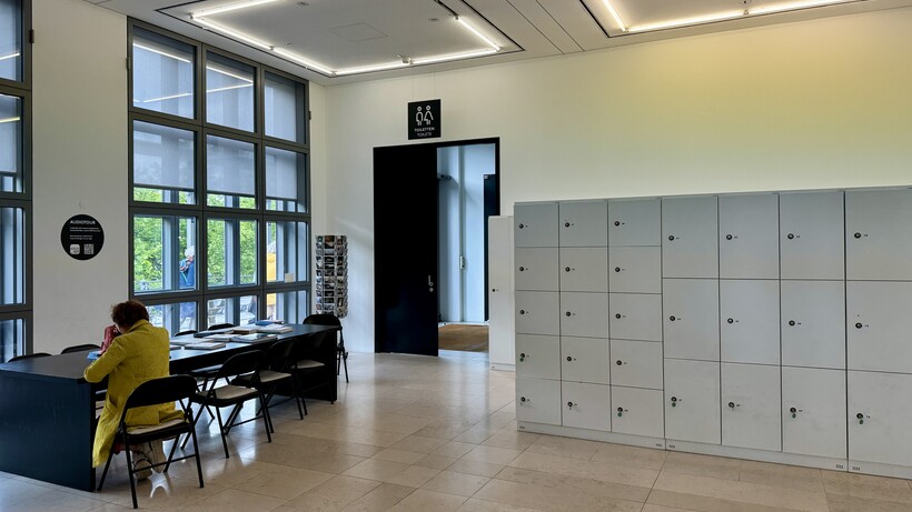 Moderne Schulaula mit Schließfächern, großen Fenstern und Schüler am Tisch