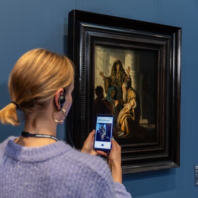 Eine Frau mit Handy und Kopfhörern vor dem Gemälde von Rembrandt Harmensz. van Rijn (1606–1669)