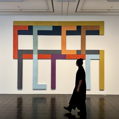 Person geht in einer Galerie vor großem bunten geometrischem Gemälde vorbei