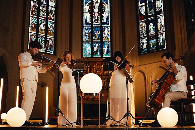 Streichquartett in einer Kirche mit beleuchteten weißen Kugeln vor bunten Glasfenstern